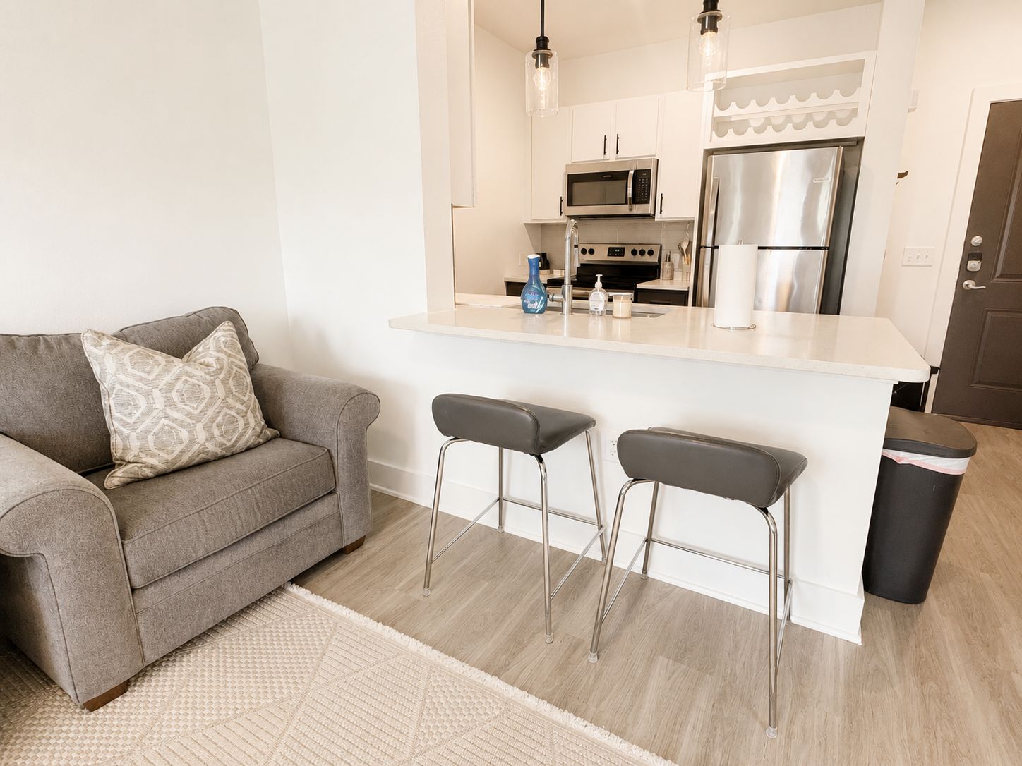 A modern kitchen with a stainless steel refrigerator, microwave, and bar stools.