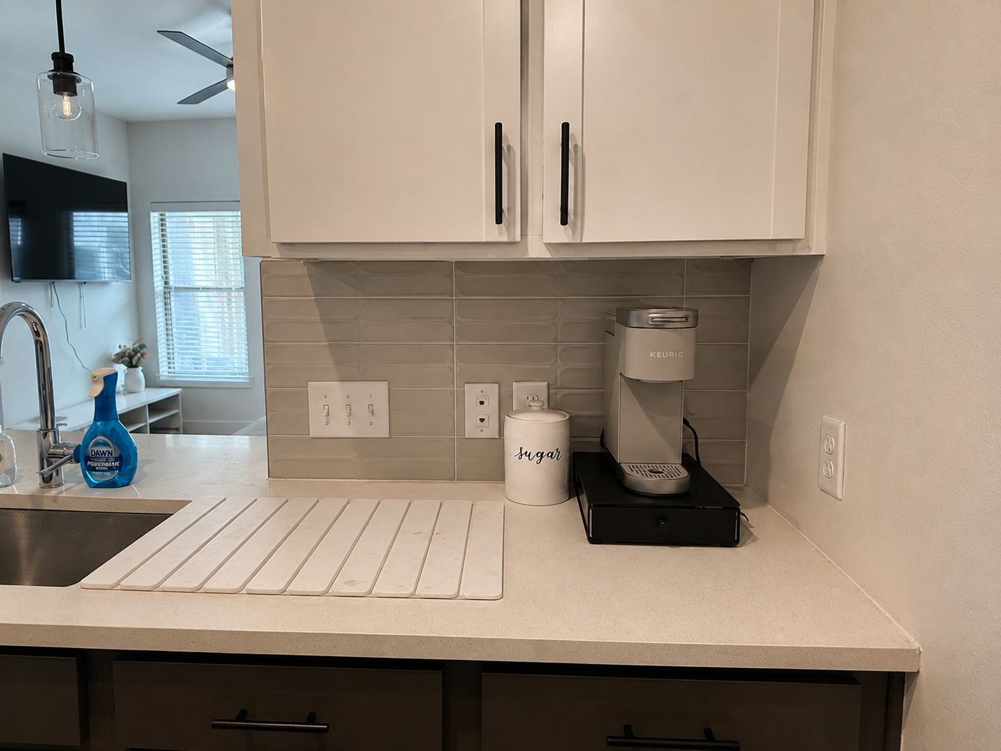 A kitchen with white cabinets, a coffee maker, a sugar container, and a Dawn dish soap bottle.