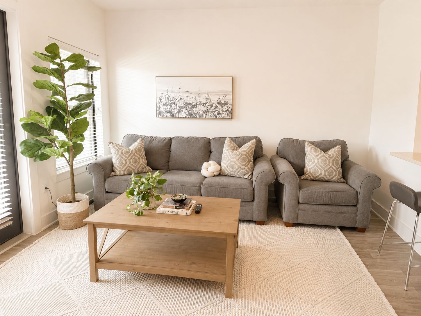 Ein Wohnzimmer mit einer Sofagarnitur, einem Couchtisch, einer Topfpflanze und einem gerahmten Bild an der Wand.