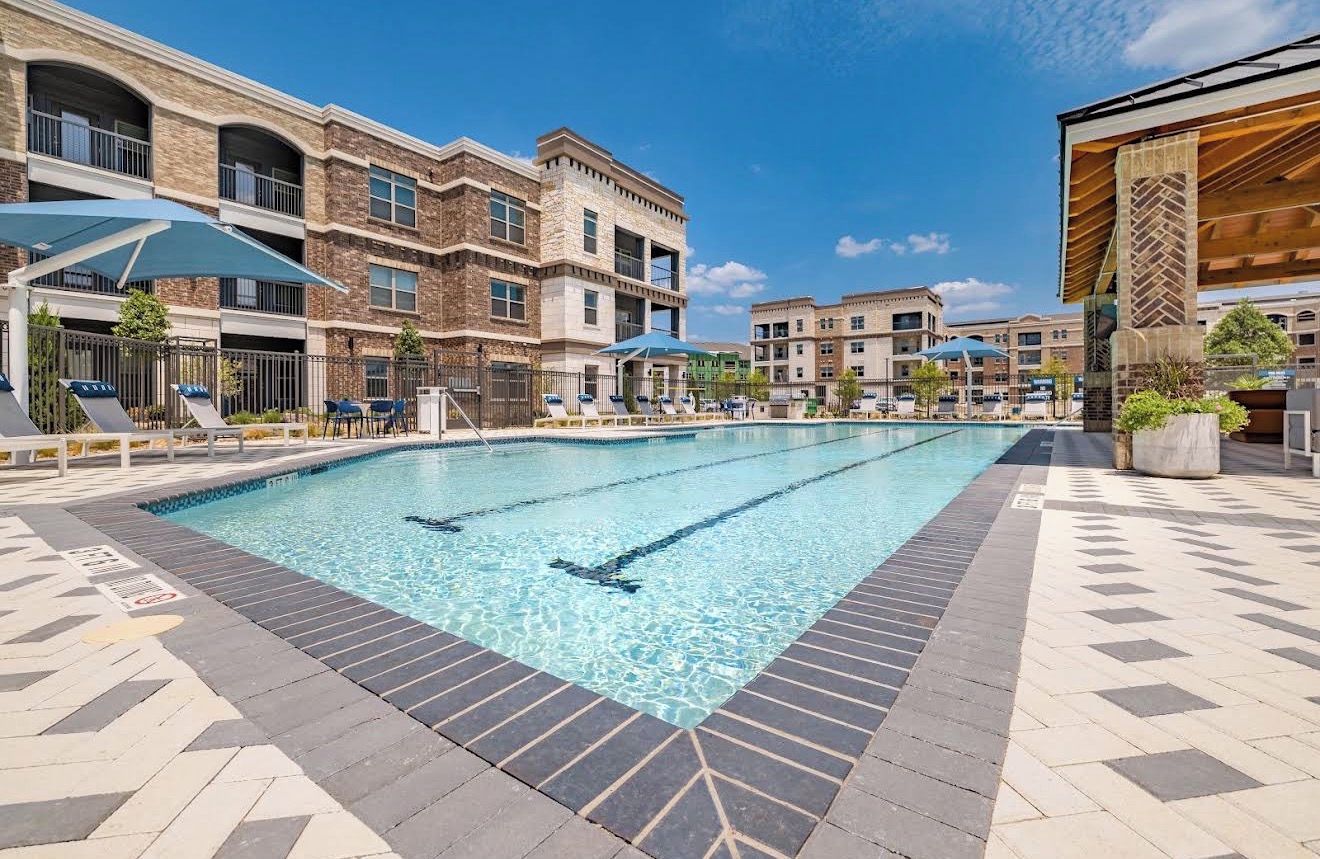 A swimming pool with lounge chairs and umbrellas, surrounded by multi-story buildings with balconies.