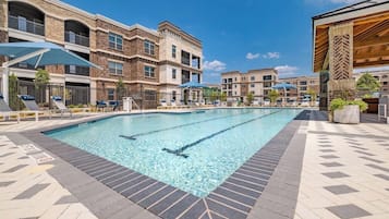 A swimming pool with lounge chairs and umbrellas, surrounded by multi-story buildings with balconies.