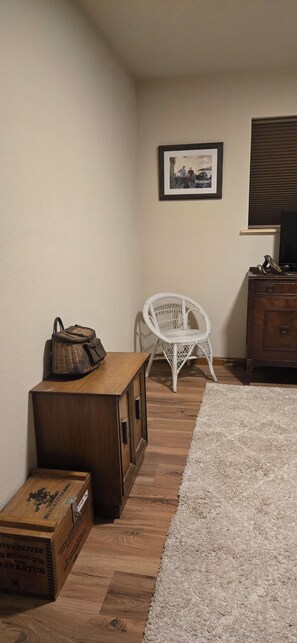 A room with a wooden chest, a wicker basket, a white wicker chair, a framed picture on the wall, and a wooden cabinet. - Adorable 3-bedroom house in pleasant Afton perfect for your getaway (Afton)