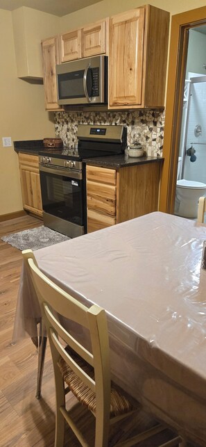 A kitchen with wooden cabinets, a microwave, an oven, and a table with a chair. - Adorable 3-bedroom house in pleasant Afton perfect for your getaway (Afton)