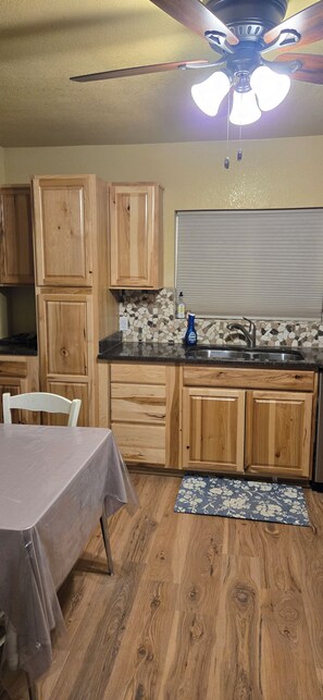 A kitchen with wooden cabinets, a tiled backsplash, a ceiling fan, and a dining table. - Adorable 3-bedroom house in pleasant Afton perfect for your getaway (Afton)