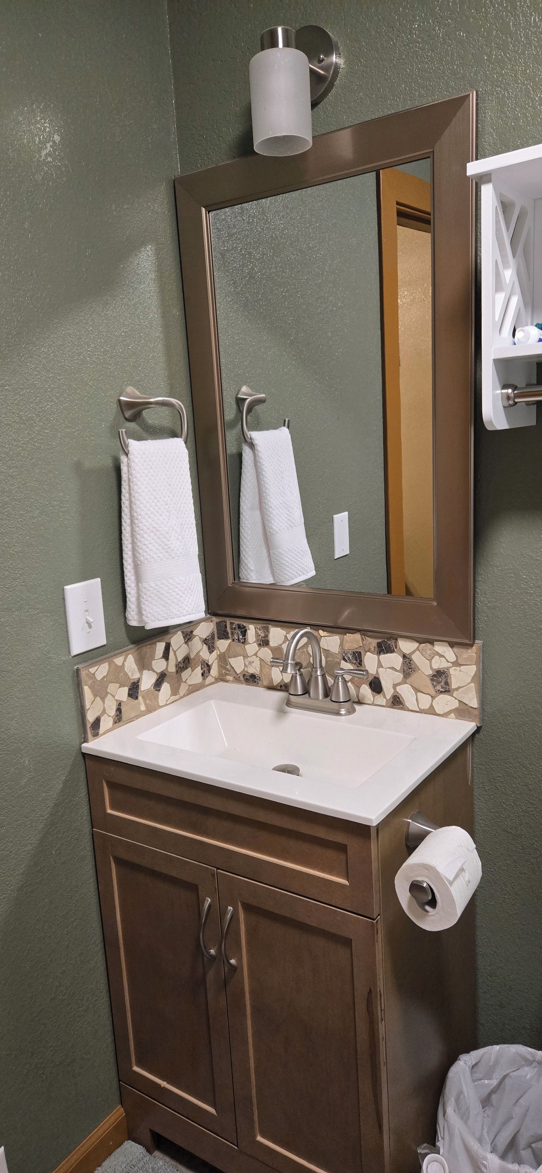 Un baño con un lavamanos blanco, un espejo, un perchero para toallas y un dispensador de papel higiénico.