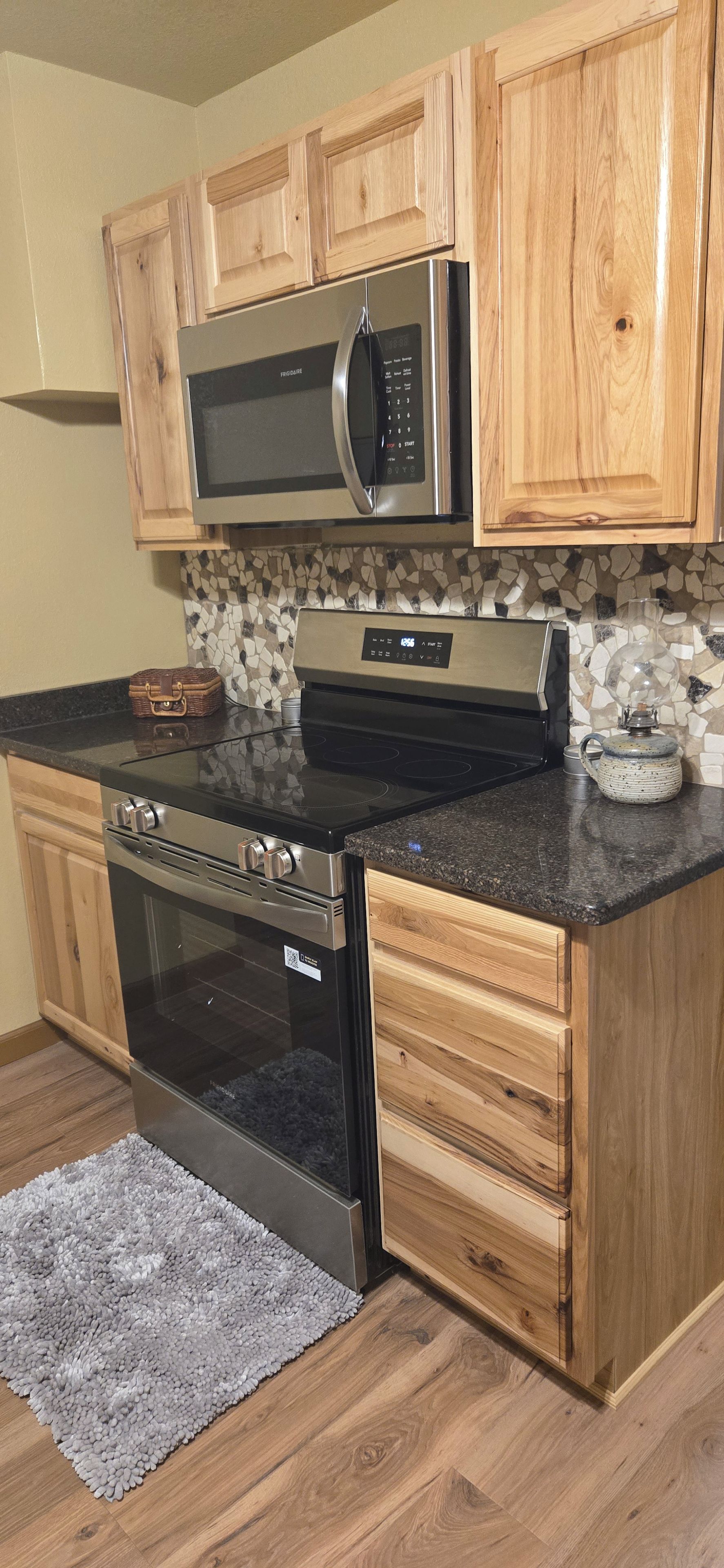 A kitchen with wooden cabinets, a stainless steel microwave, a stove, and a granite countertop.