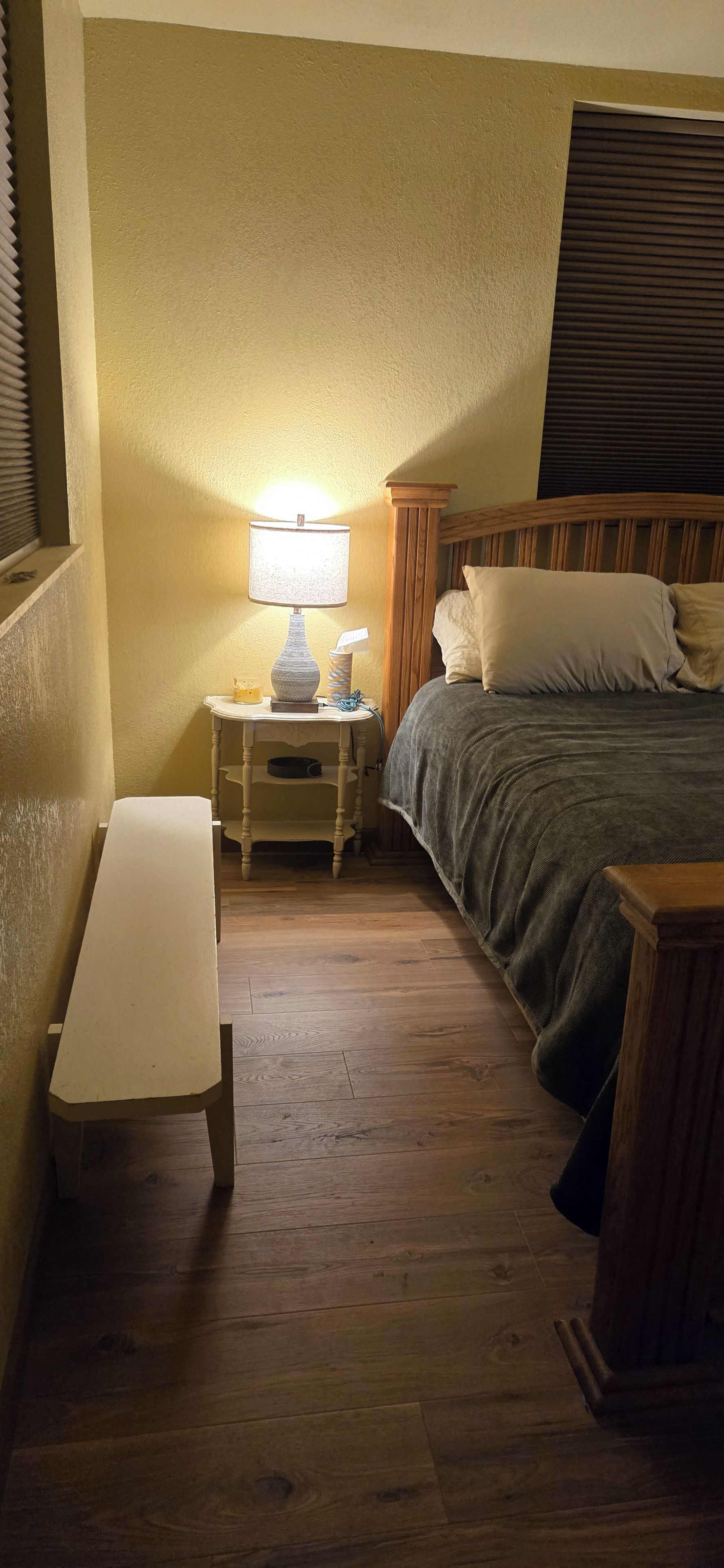 A bedroom with a bed, bedside table, lamp, and a bench.