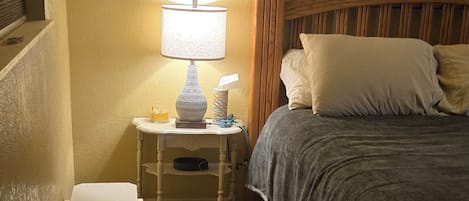 A bedroom with a bed, bedside table, lamp, and a bench.
