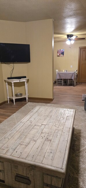 A room with a wooden table, a television mounted on the wall, and a dining area with chairs and a table. - Adorable 3-bedroom house in pleasant Afton perfect for your getaway (Afton)