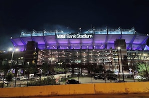 M&T Bank Stadium with a large, illuminated sign, multiple levels of seating, and a parking area in the foreground.