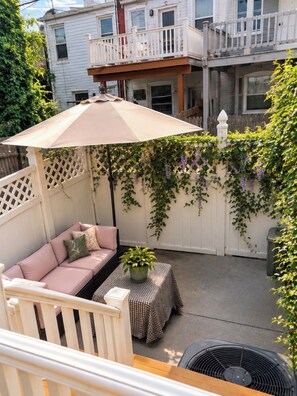 A covered patio area with a cushioned seating arrangement, a table with a checkered tablecloth, and a potted plant.