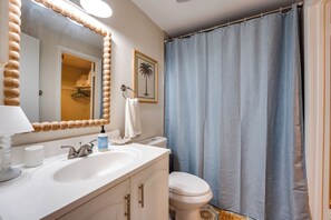 Un baño con lavamanos blanco, un espejo con marco de madera, inodoro y cortina de ducha.