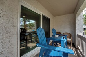 Ein überdachter Außenbereich mit blauen Adirondack-Stühlen und einem Tisch, mit Blick auf ein Schwimmbad und Palmen.