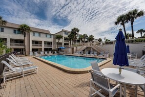 Zona de piscina con sillones reclinables, mesa de billar y una escalera que lleva a un edificio.