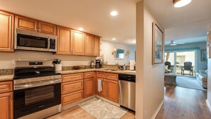 A modern kitchen with wooden cabinets, stainless steel appliances, and a granite countertop. - 2-bedroom Condo in St. Augustine- Private Beach Beach Access + Pool! (St. Augustine)