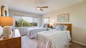 A bedroom with two beds, a ceiling fan, and a large window with a view of palm trees. - 2-bedroom Condo in St. Augustine- Private Beach Beach Access + Pool! (St. Augustine)
