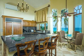 A kitchen with a granite countertop, wooden chairs, and a view of the ocean through large windows. - Villa Paraiso Ocean front 8-bedroom Villa in Palmilla Sur Private beach (Palmilla)