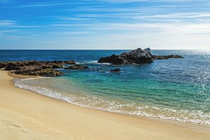 Een strand met helderblauw water, een zandstrand en rotsformaties.