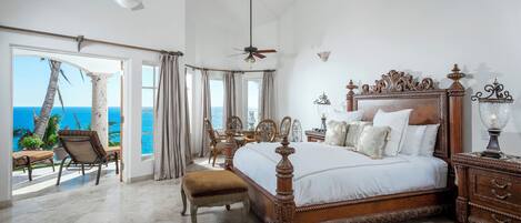 Une chambre spacieuse avec un grand lit, un ventilateur de plafond et une vue sur l’océan.
