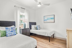 A room with two beds, a nightstand, a lamp, and a painting on the wall. - Tan Lines and Fine Wines (Port Aransas)