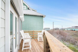 A wooden deck with two white chairs, a wooden railing, and a view of the surrounding area. - Tan Lines and Fine Wines (Port Aransas)