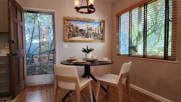 A dining area with a round table, two chairs, a chandelier, and a window with blinds.