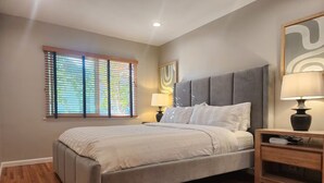 Ein Schlafzimmer mit einem Bett, Nachttisch, Lampe und Fenster mit Jalousien.