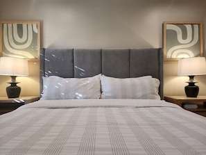 A bed with a grey upholstered headboard, two bedside lamps, and two abstract paintings on the walls. - Comfy Courtyard 1 Bedroom at Jackson Market (Culver City)