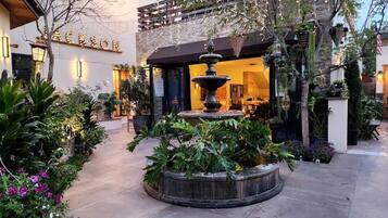 A courtyard with a fountain, potted plants, and a building with a sign.