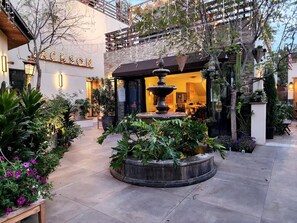 A courtyard with a fountain, potted plants, and a building with a sign. - Comfy Courtyard 1 Bedroom at Jackson Market (Culver City)