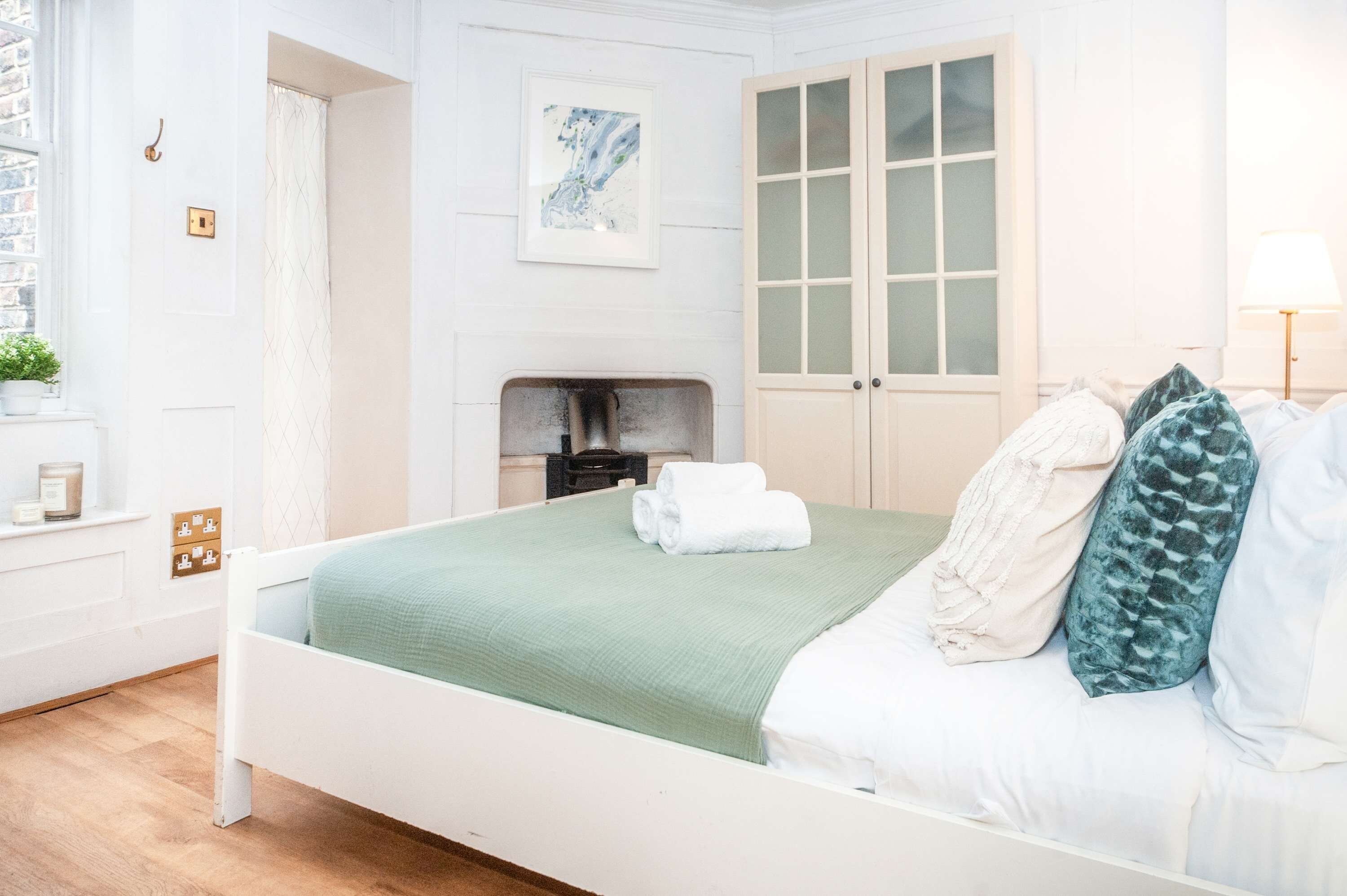 Un dormitorio ordenado con cama, mesita de noche, lámpara, ventana y puerta.