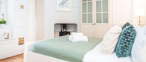 Un dormitorio ordenado con cama, mesita de noche, lámpara, ventana y puerta.