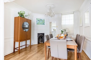 A dining area with a wooden table, grey upholstered chairs, a chandelier, and a fireplace. - Spacious 3BR 2BA Home in the Heart of Soho (London)