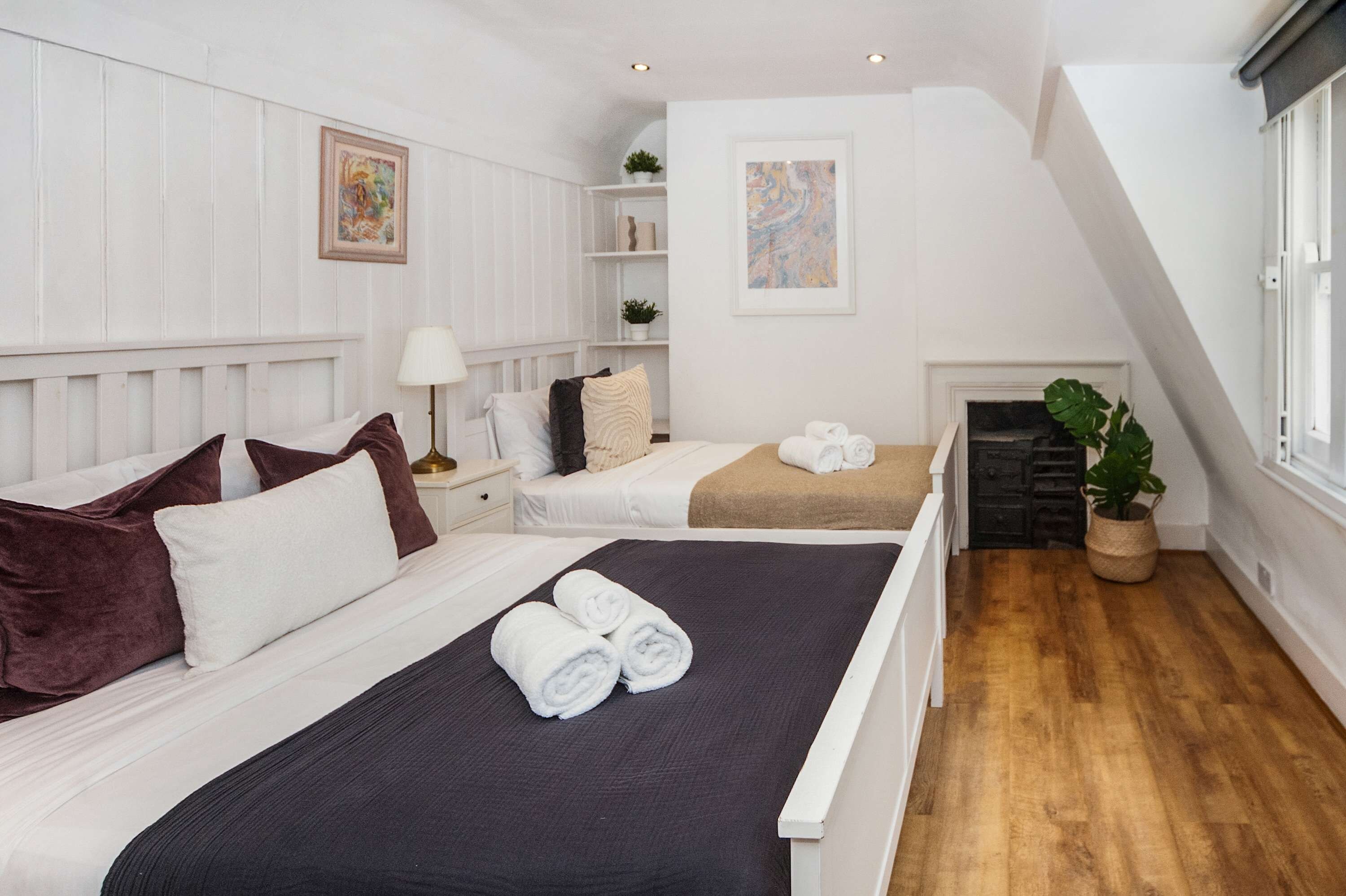 A bedroom with two beds, a fireplace, and a potted plant.