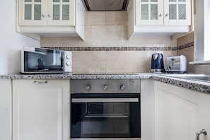 A kitchen with white cabinets, a microwave, a toaster, and an oven. - Spacious 3BR 2BA Home in the Heart of Soho (London)