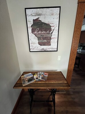 A framed map of Wisconsin with the word 'home' on a wall-mounted table with magazines. - Beautifully Renovated Farmhouse next to Dorf Haus Supper Club (Sauk City)
