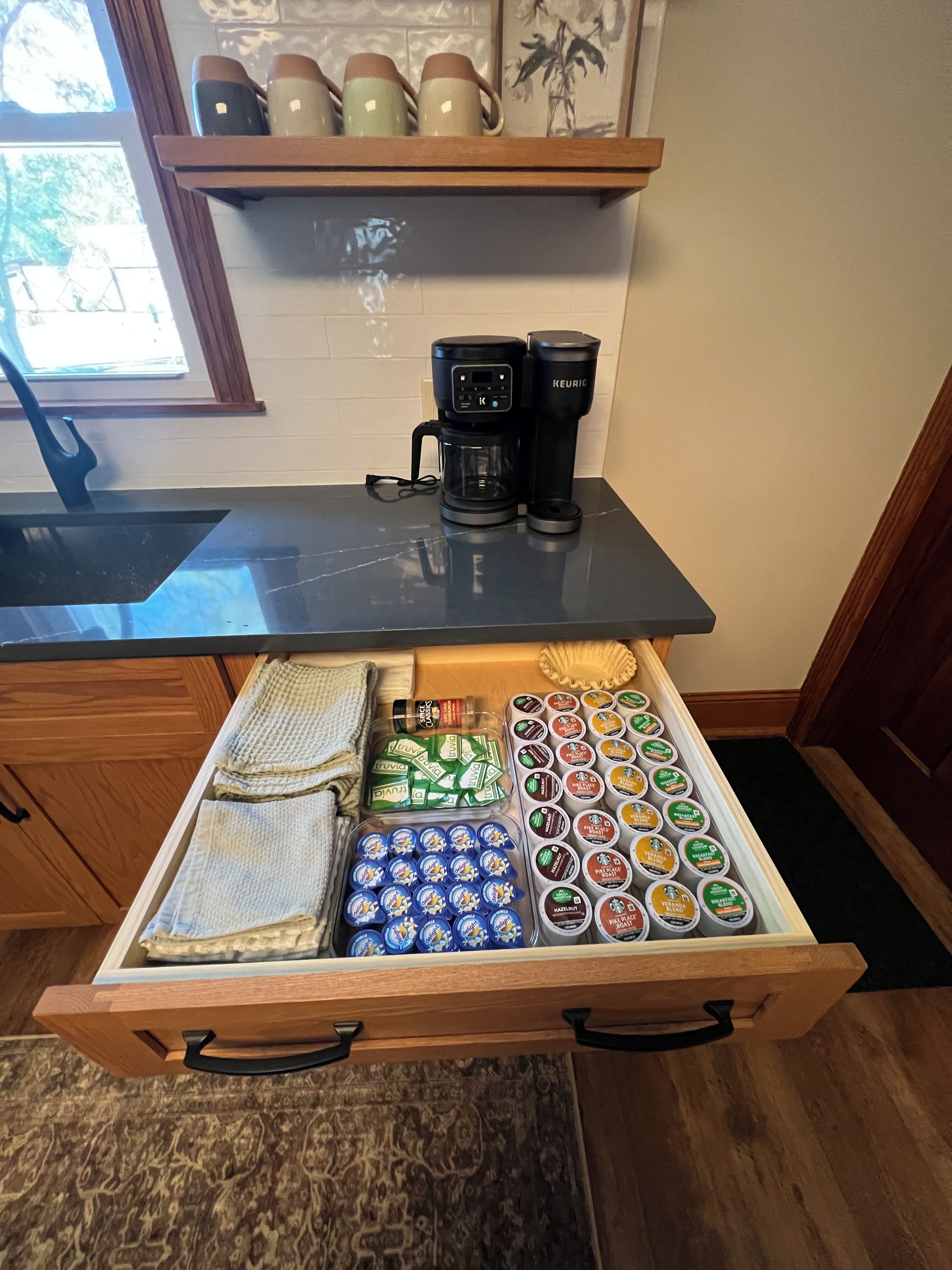 A kitchen counter with a coffee maker and a drawer filled with food items.