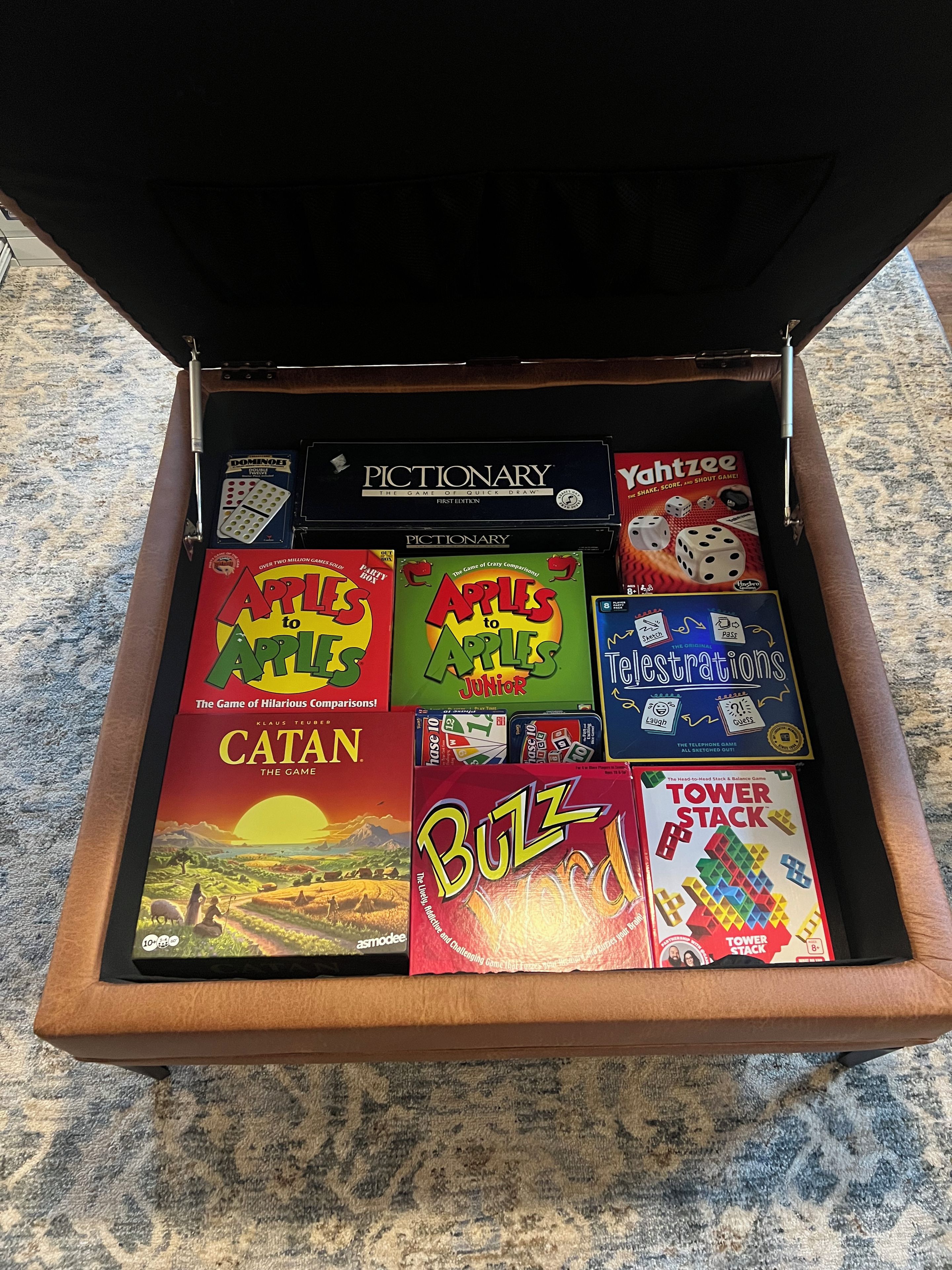 A drawer with various board games including Catan, Apples to Apples, and Pictionary.