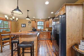A kitchen with wooden cabinets, a stainless steel refrigerator, and a bar area with stools. - Mineral Mountain Lodge in Gilded Mountain (Lead)