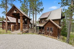 A rustic cabin with a wooden porch and a metal roof, surrounded by tall pine trees. - Mineral Mountain Lodge in Gilded Mountain (Lead)