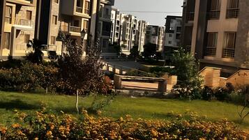 A residential building with multiple balconies, a paved pathway, and a garden with yellow flowers.