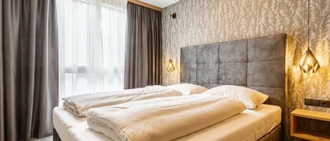 A hotel room with a large bed, curtains, a headboard, and wall-mounted lighting.