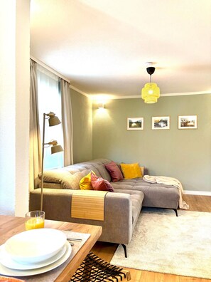 A cozy living room with a sofa, a dining table with plates and a glass of orange juice, and a wall with framed pictures. - Cozy & central appartement with 3 bed rooms (Bad Kohlgrub)
