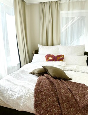 A hotel room with a bed, white bedding, a patterned throw blanket, and sheer curtains. - Cozy & central appartement with 3 bed rooms (Bad Kohlgrub)