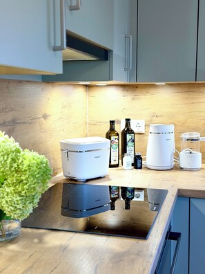 Et køkken med moderne design, der indeholder en indbygget ovn, kaffemaskine og blender på bordpladen.