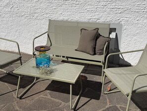 A metal-framed outdoor seating area with a glass-top table, a bottle of blue liquid, and a decorative item. - Cozy & central appartement with 3 bed rooms (Bad Kohlgrub)