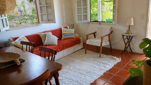 A cozy living room with a red sofa, a wooden chair, a dining table, and a white rug.
