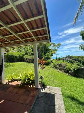 A covered outdoor area with a view of a lush green landscape and a distant view of houses.