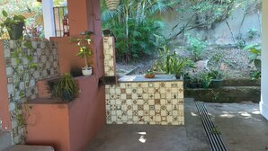 Uma área com bancos azulejados e plantas em vasos, parede revestida com desenhos decorativos e piso de concreto.
