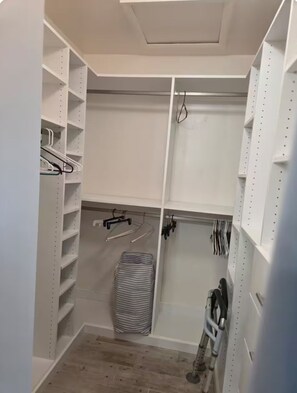 En rymlig klädkammare med öppna hyllor, en torkställning och en rullstol.